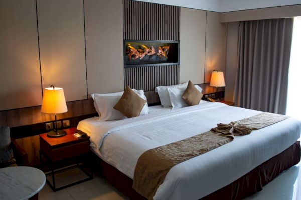 A cozy hotel room with a large bed, pillows, side tables with lamps, and a decorative fireplace on the wall.