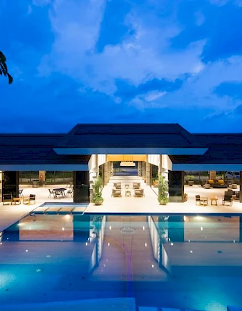 A luxurious building with an illuminated pool at night, surrounded by seating areas and a clear sky above.