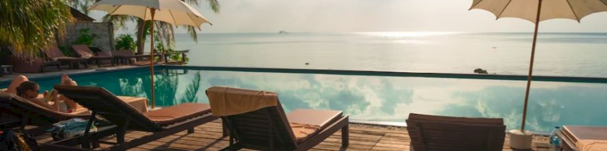 A serene poolside scene with lounge chairs, umbrellas, and a view of a calm sea under a bright sky.