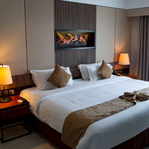 A cozy hotel room with a large bed, two lamps, decorative pillows, and a small table next to it, featuring warm lighting and curtains.