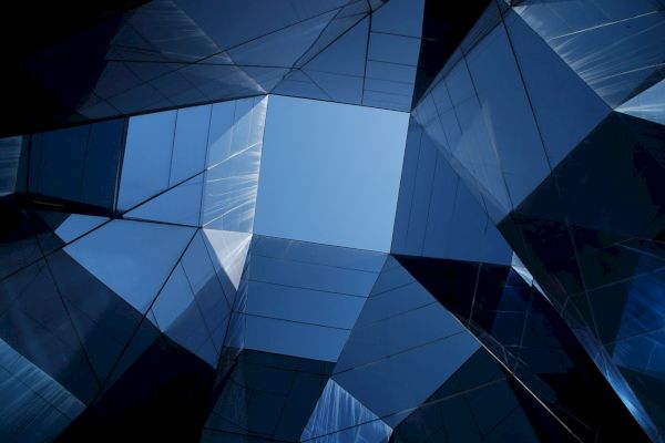 View of a geometric, mirrored architectural structure with a blue sky visible through a central opening.