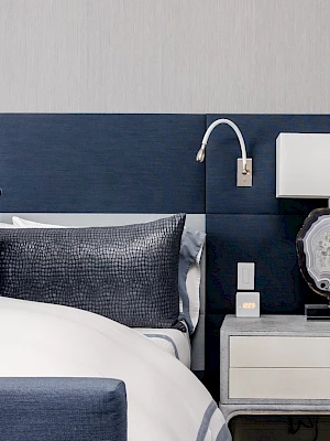 A stylish bedroom features a bed with blue accents, a modern wall-mounted lamp, and a nightstand with a decorative lamp and accessories.