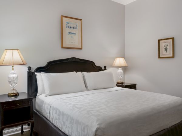 A neatly made bed with white linens, two bedside tables with lamps, and framed artwork above, all in a softly lit, neutral-toned room.