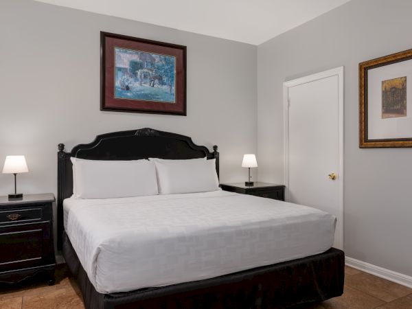 A neatly made bed with white linens and two bedside tables, each with a lamp, in a room with two framed artworks on gray walls.