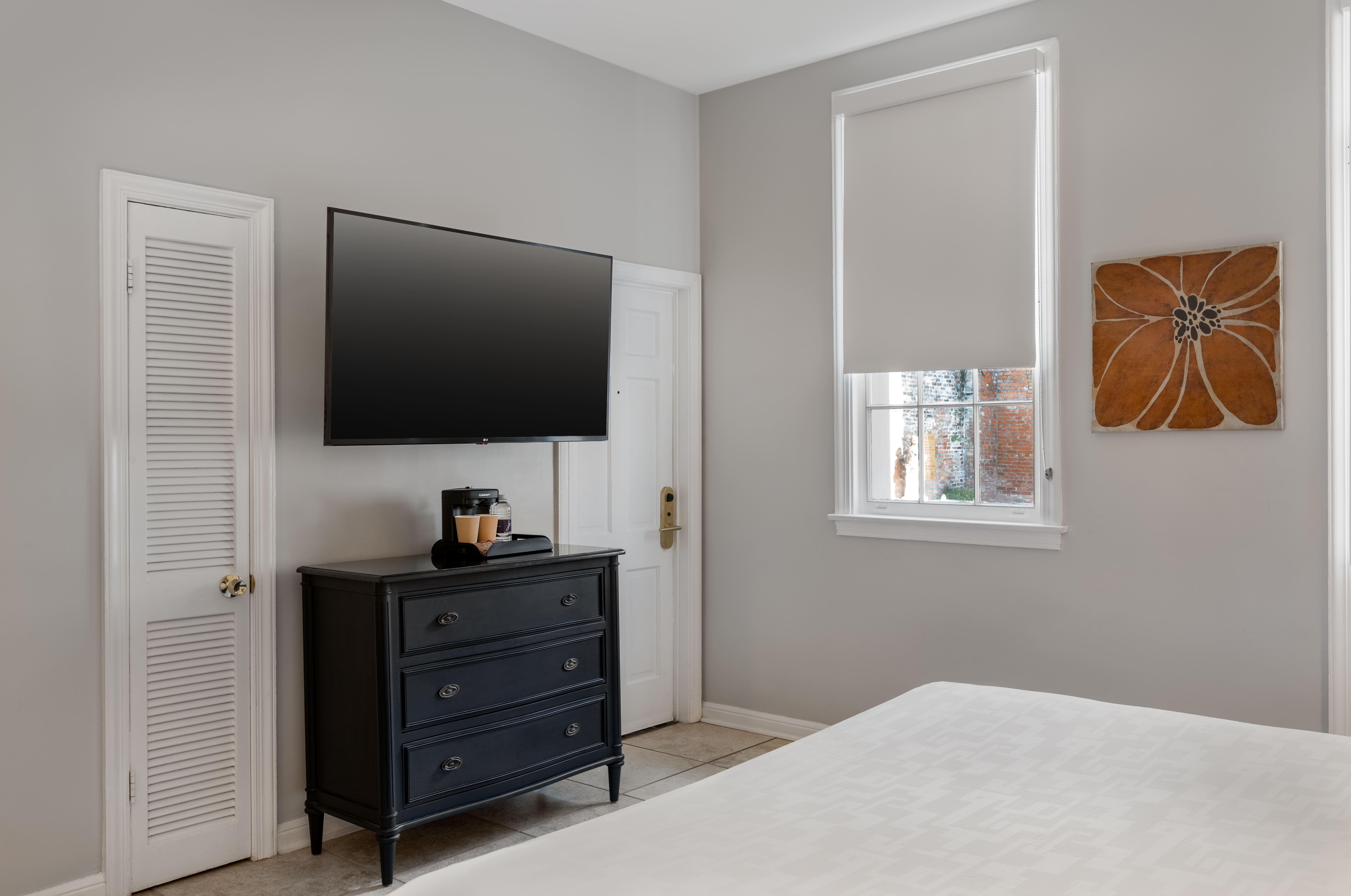 A hotel room with a large bed, TV, dresser, and window