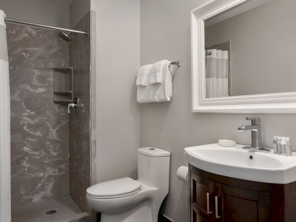 A modern bathroom with a shower, toilet, vanity with sink, mirror, and neatly hung towels on a rack.
