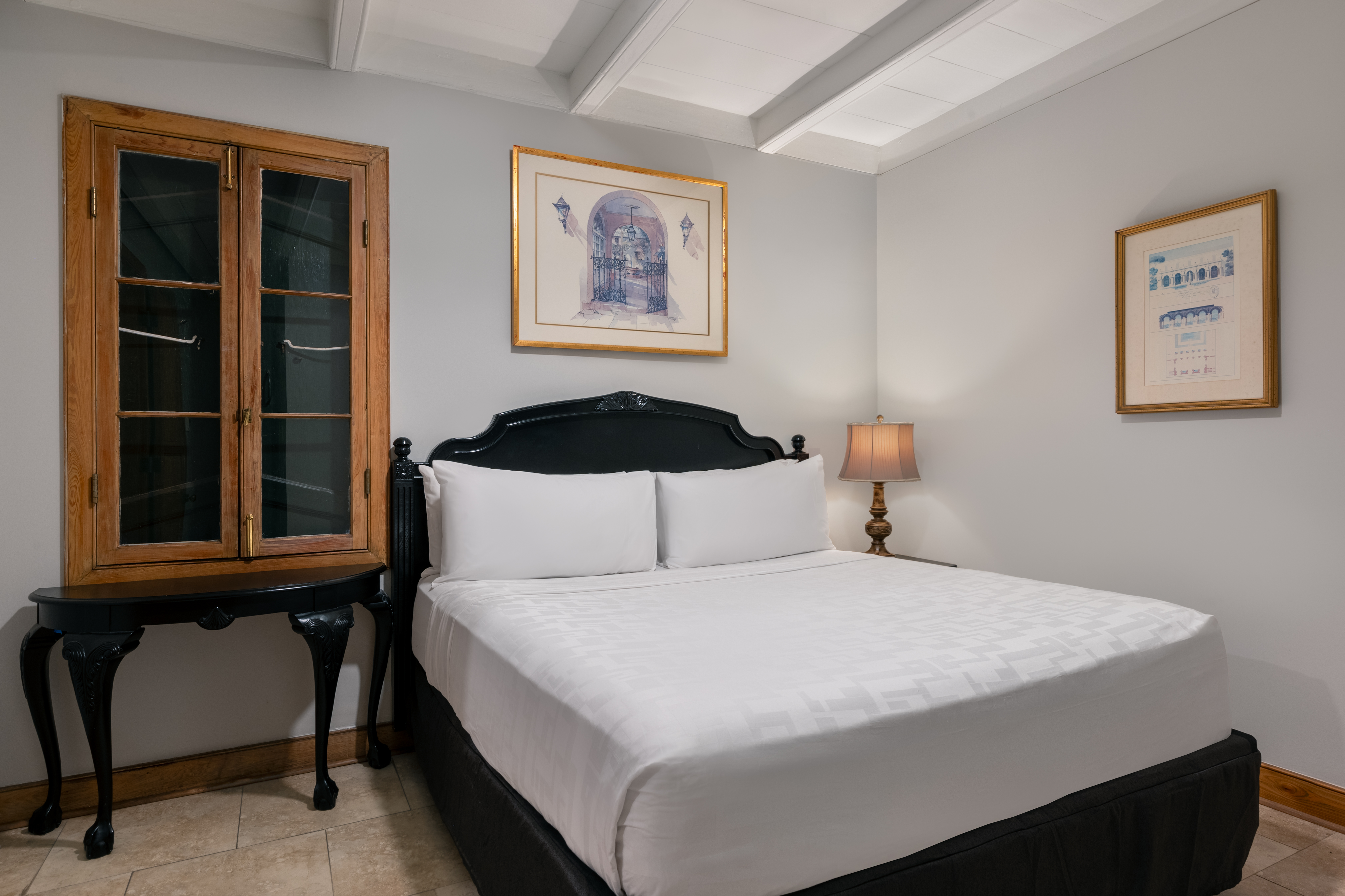 A neatly made bed with white linens in a room with gray walls, a wooden window, and framed artwork.