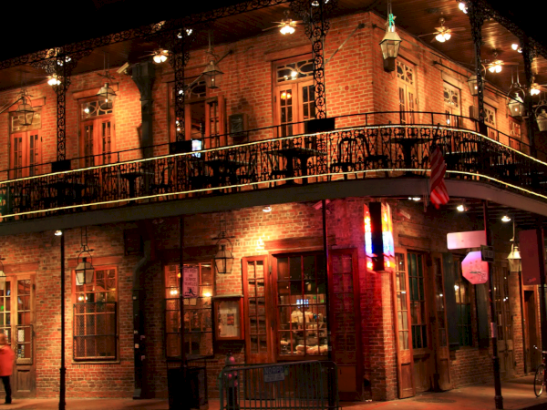 A brick corner pub at night with warm lights, two levels, balconies, and people walking by. (140 chars, ending with a period)