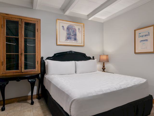 A hotel room with a large bed, wooden cabinet, and framed artwork on the walls.