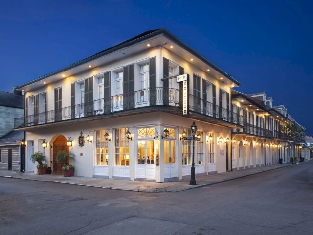 A two-story white building with black balustrades and lights on, taken at dusk.