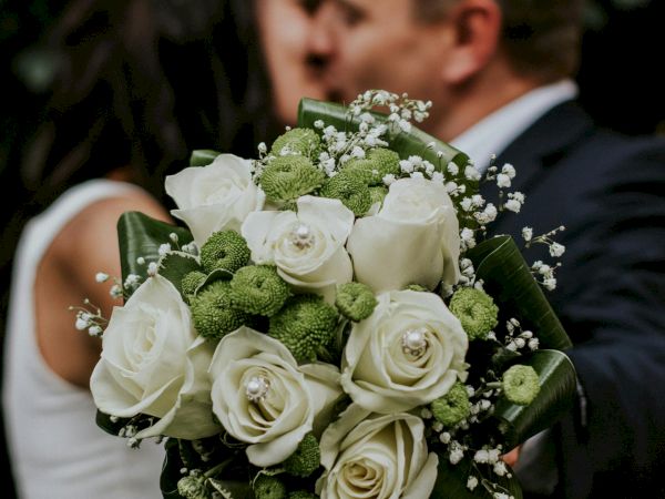 A couple is kissing, with a focus on a bouquet of white and green flowers in the foreground, creating a romantic scene.