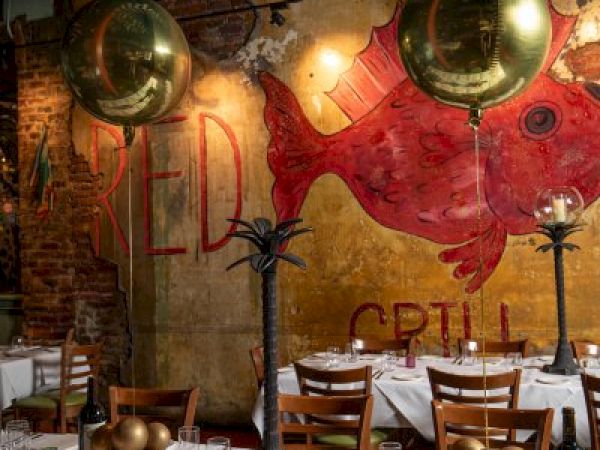 A restaurant interior with decorated tables, gold balloons, and a mural of a red fish on the wall, creating a festive atmosphere.