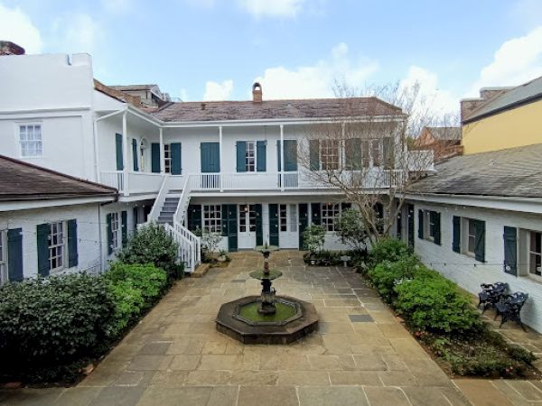 The image shows a courtyard with a central fountain, surrounded by a two-story building with doors and windows.