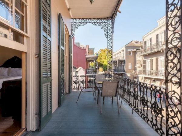 A balcony with decorative railings overlooks a street with classic architecture. There's a table and chairs set up on the balcony.