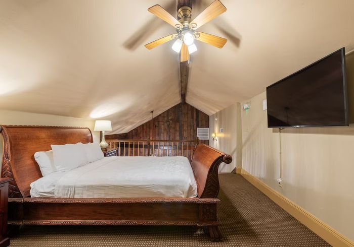 A wide-angle view of a hotel room with a large bed, TV, and ceiling fan.