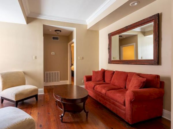 A cozy living room with a red sofa, armchairs, a wooden coffee table, and a large wall mirror in a neutral-toned interior.