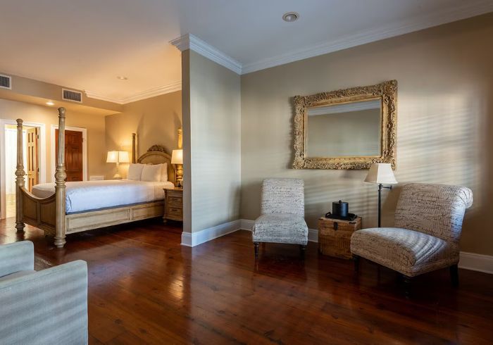 A wide view of a hotel room with a four-poster bed, two armchairs, and a mirror on the wall.