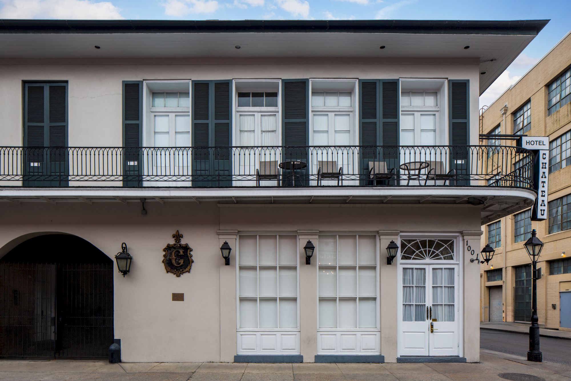A two-story building with white doors and windows, black shutters, a balcony on the upper floor, and a street sign on the right.