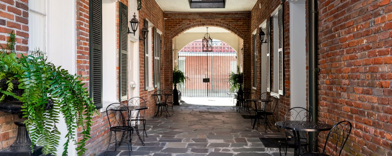 A brick courtyard with an archway, outdoor seating, and plants.