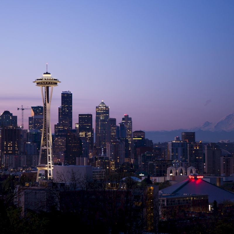 A cityscape at dusk with a skyline including a tower and a distant mountain, under a gradient sky.