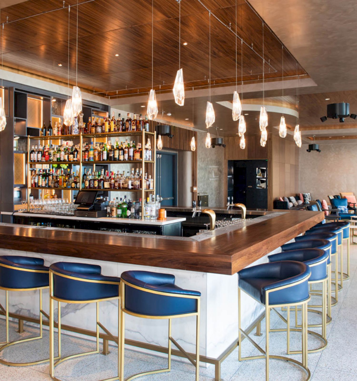 A modern bar with stylish seating, pendant lights, and a well-stocked counter in a spacious, chic setting, featuring various seating areas.