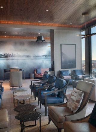 A modern lounge with plush seating, a mural, and large windows showcasing a waterfront view with a Ferris wheel in the distance.