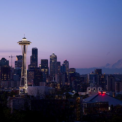The image shows the Seattle skyline at dusk, featuring the Space Needle and surrounding skyscrapers with Mount Rainier in the background.