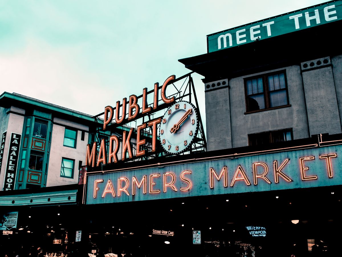 Neon signs reading "Public Market" and "Farmers Market" with a clock are visible on buildings. It's a well-known market location.