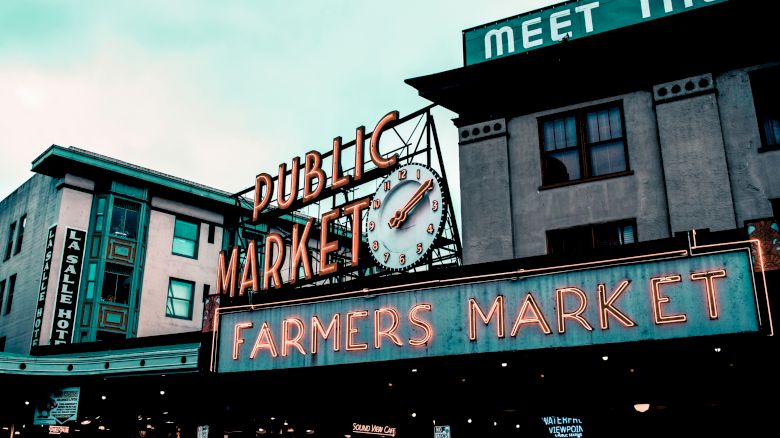 Neon signs reading "Public Market" and "Farmers Market" with a clock are visible on buildings. It's a well-known market location.